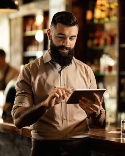 Young smiling waiter using touchpad while working in a pub.